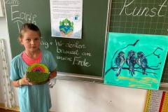 Kind steht neben der Tafel und zeigt ihr Meisterwerk.