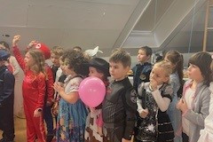 Kinder in Kostümen halten bunte Ballons und lächeln fröhlich in die Kamera.