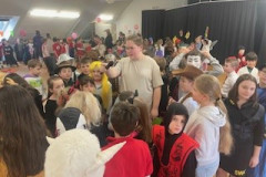 Eine Gruppe von Kindern in Kostümen steht um eine Frau in der Mitte, alle lächeln und haben Spaß.