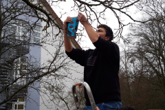 Ein Mann hängt ein Futterhäuschen an einem Baum auf.