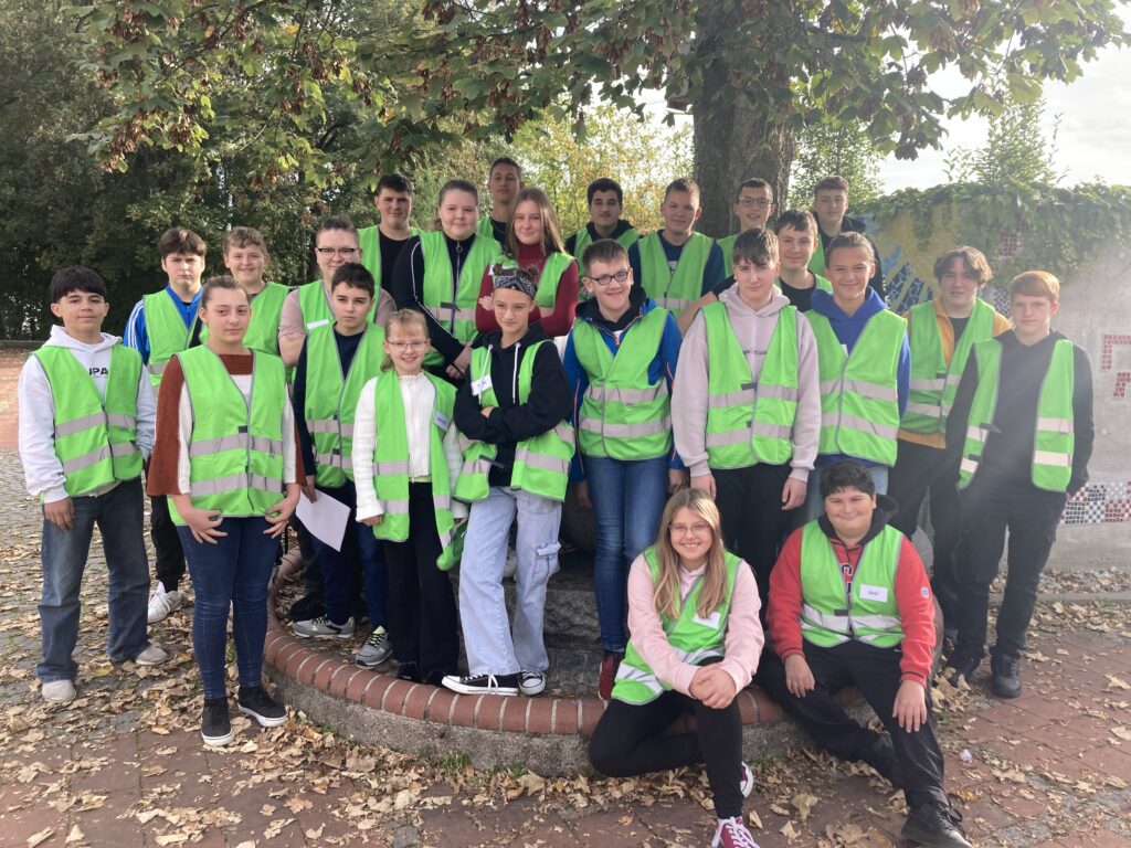 Gemeinsam sind wir stark! Kinder Gruppenbild mit grünen Warnwesten an einem Baum.